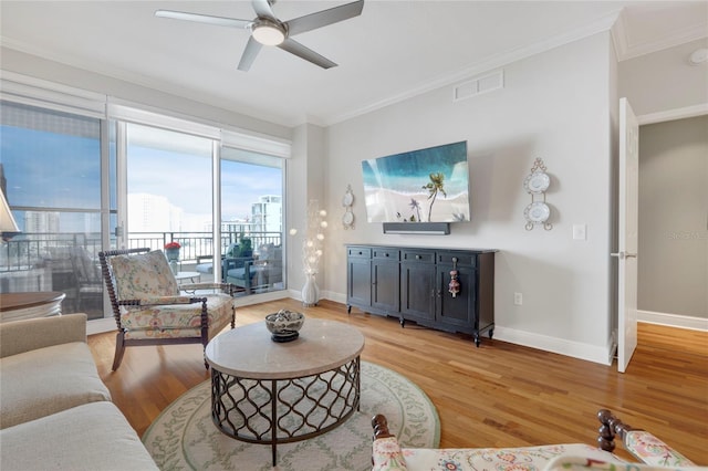 living area with ornamental molding, light wood-type flooring, visible vents, and baseboards