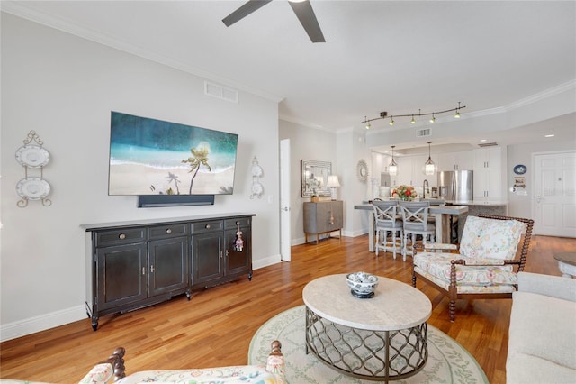 living area with visible vents, baseboards, a ceiling fan, light wood-style flooring, and ornamental molding