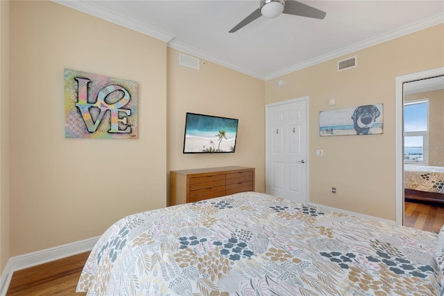 bedroom with baseboards, wood finished floors, visible vents, and crown molding