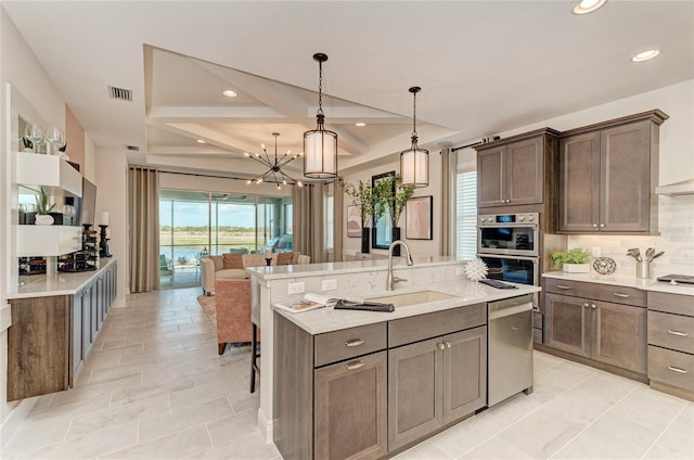 kitchen with a center island with sink, appliances with stainless steel finishes, sink, hanging light fixtures, and tasteful backsplash