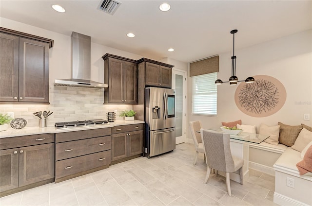 kitchen featuring stainless steel appliances, breakfast area, dark brown cabinets, wall chimney range hood, and pendant lighting