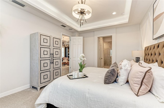 bedroom featuring a tray ceiling, light carpet, and ensuite bathroom