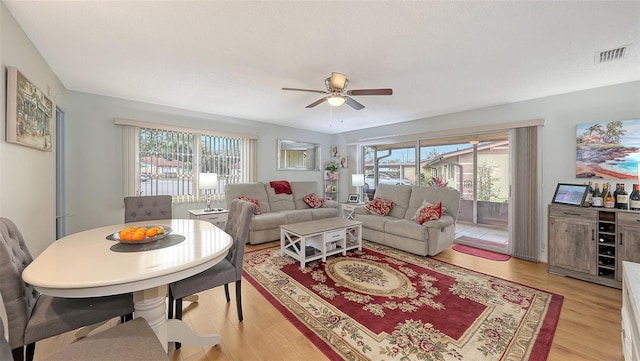 living room featuring light wood-style floors, visible vents, plenty of natural light, and a ceiling fan