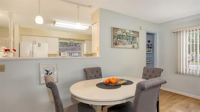 dining room featuring light wood-style flooring, baseboards, and a textured ceiling