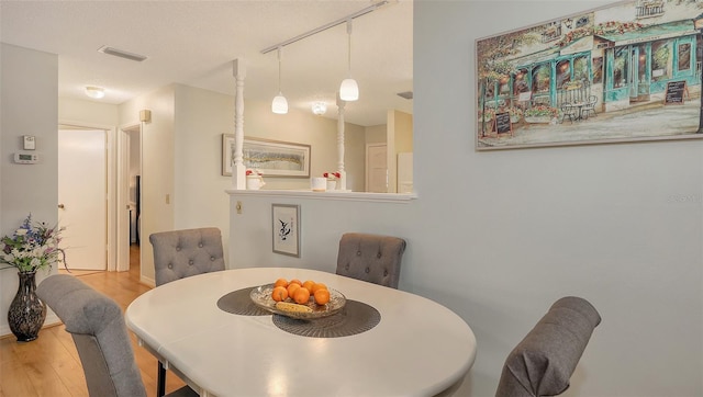 dining room with light wood-style floors, visible vents, and track lighting