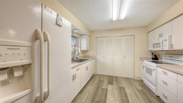 kitchen with white appliances, light countertops, a sink, and white cabinetry