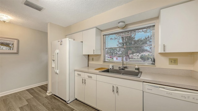 kitchen with white appliances, a sink, visible vents, white cabinets, and light countertops