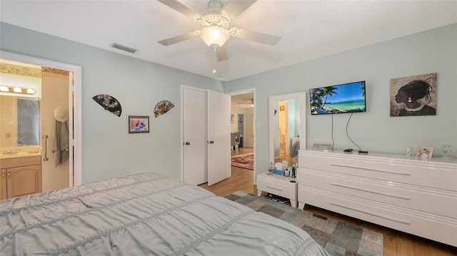 bedroom with visible vents, ceiling fan, ensuite bathroom, a textured ceiling, and light wood-style floors