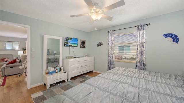 bedroom with ceiling fan, a textured ceiling, baseboards, and wood finished floors