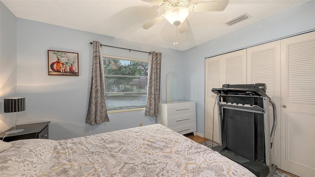 bedroom with a textured ceiling, ceiling fan, visible vents, a closet, and dark wood-style floors