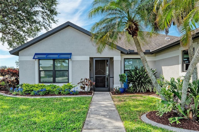 view of front of property featuring stucco siding, a front yard, and a shingled roof