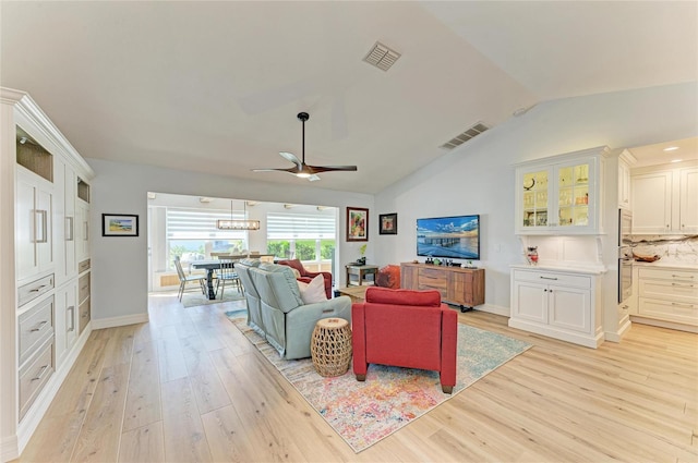 living area featuring lofted ceiling, a ceiling fan, visible vents, and light wood finished floors