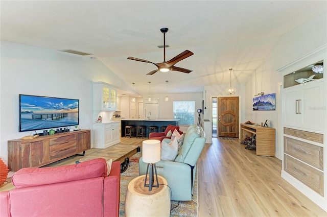 living area with visible vents, light wood-style floors, ceiling fan, and vaulted ceiling