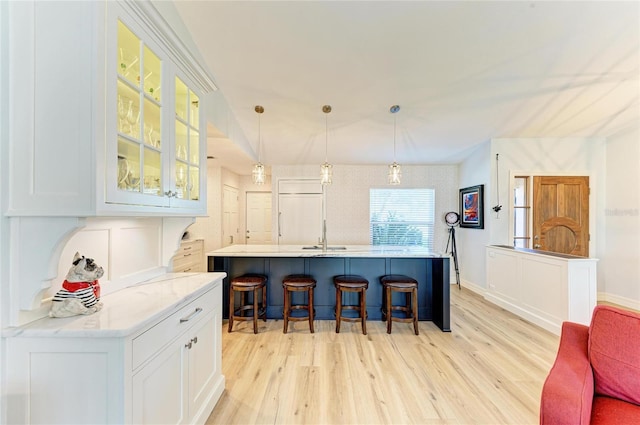 kitchen featuring a breakfast bar, paneled built in fridge, glass insert cabinets, and light wood finished floors