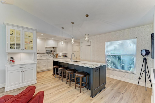 kitchen featuring wallpapered walls, lofted ceiling, a kitchen breakfast bar, paneled built in refrigerator, and a sink