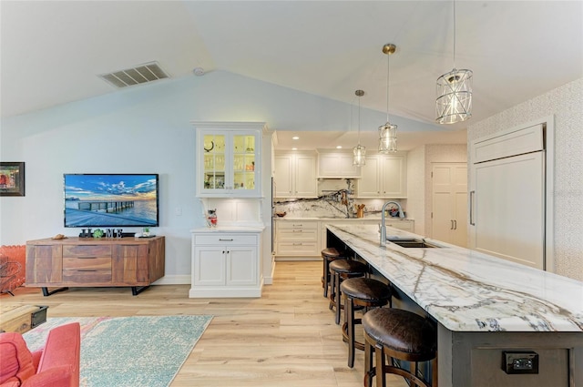 kitchen featuring visible vents, a breakfast bar, a sink, paneled built in fridge, and light wood-style floors