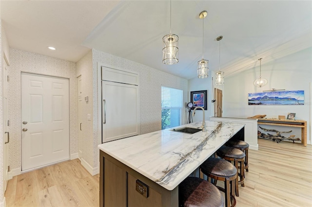 kitchen with wallpapered walls, baseboards, light stone counters, light wood-style flooring, and a sink