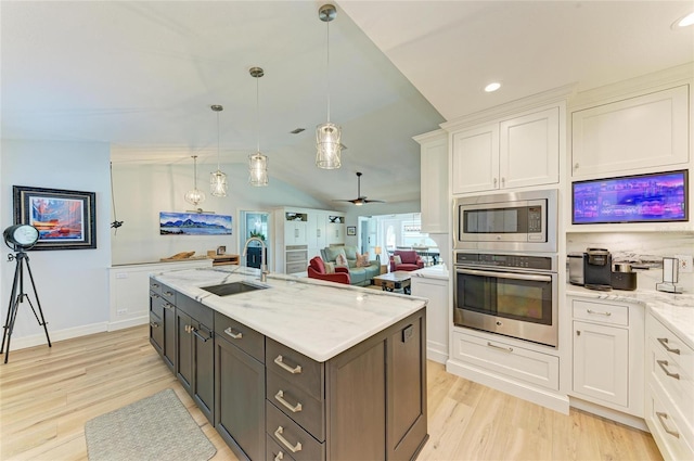 kitchen with a sink, light stone counters, appliances with stainless steel finishes, and white cabinetry