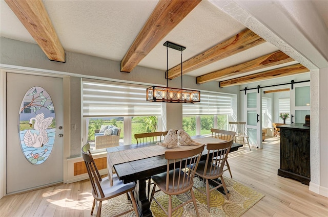 dining space with a barn door, beam ceiling, and light wood-style flooring