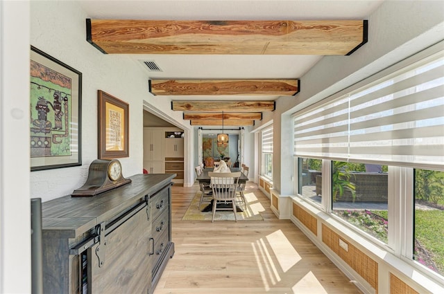 hallway with beamed ceiling, visible vents, light wood finished floors, baseboards, and a textured wall