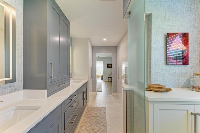 bathroom featuring tile patterned flooring, a sink, wallpapered walls, and double vanity