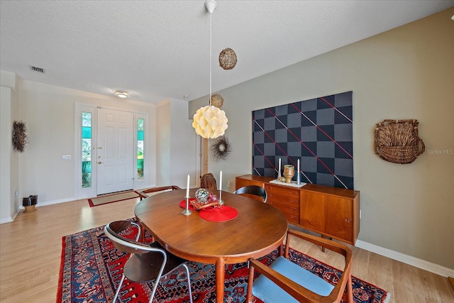 dining space featuring light wood-type flooring and a textured ceiling