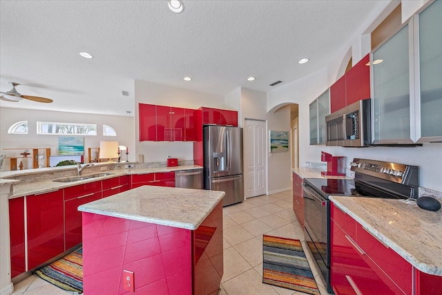 kitchen featuring stainless steel appliances, a kitchen island, light stone countertops, and sink