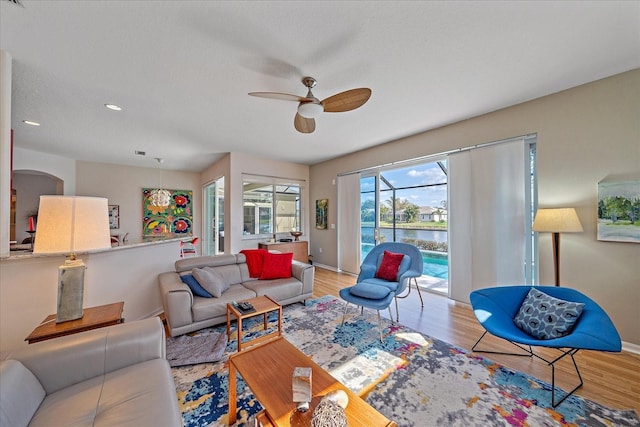 living room featuring a water view, light hardwood / wood-style flooring, ceiling fan, and a textured ceiling