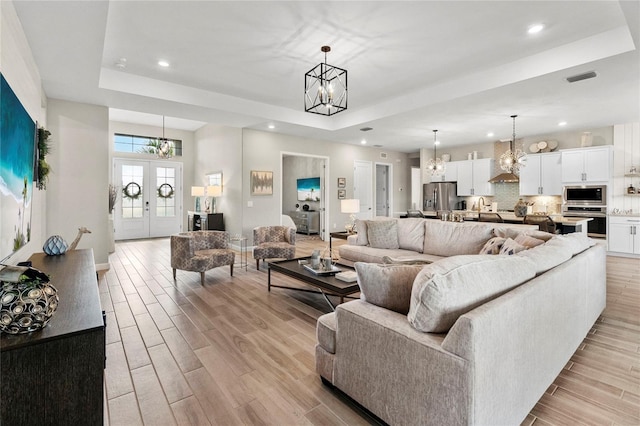 living room with a raised ceiling, light hardwood / wood-style floors, and an inviting chandelier