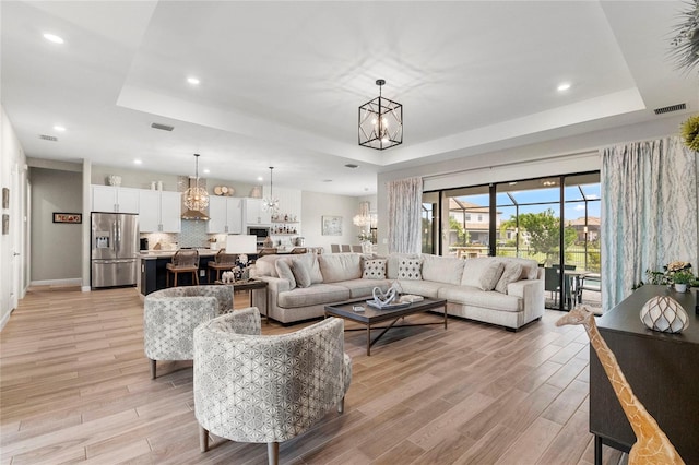 living room featuring light wood-type flooring, a chandelier, and a raised ceiling