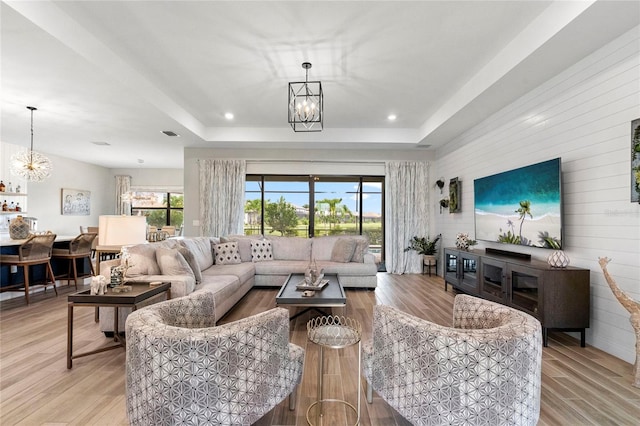 living room featuring a tray ceiling, an inviting chandelier, and light hardwood / wood-style floors