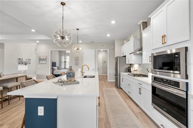 kitchen featuring appliances with stainless steel finishes, a center island with sink, hanging light fixtures, white cabinetry, and a kitchen bar