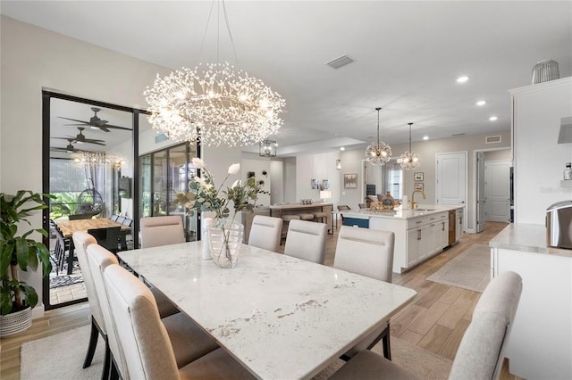 dining space with ceiling fan with notable chandelier, sink, and light hardwood / wood-style floors