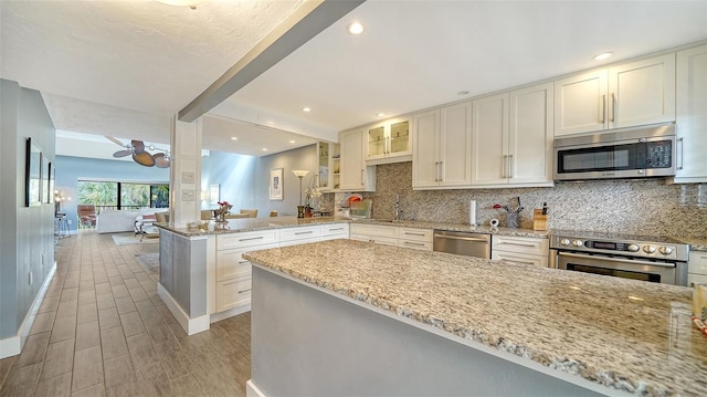 kitchen featuring light stone counters, light wood finished floors, stainless steel appliances, tasteful backsplash, and a peninsula