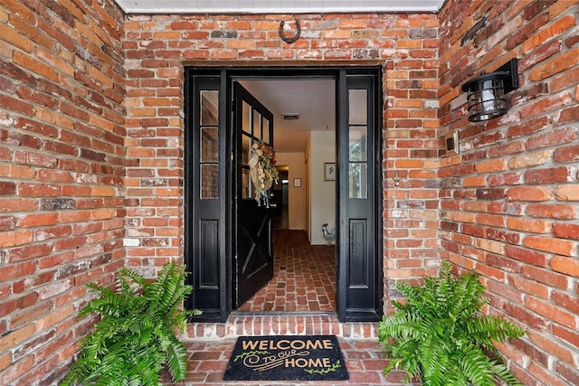 view of exterior entry featuring visible vents and brick siding