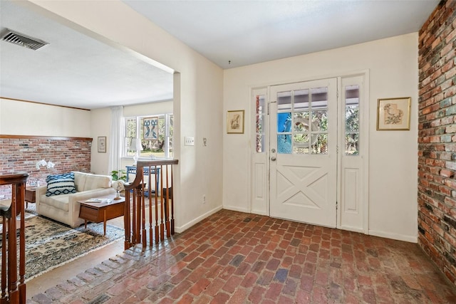 foyer featuring brick floor, baseboards, brick wall, and visible vents