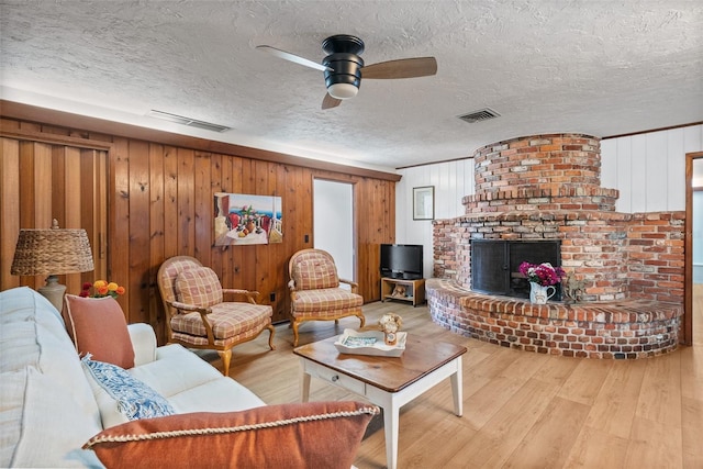 living room with a textured ceiling, light wood finished floors, a brick fireplace, and visible vents