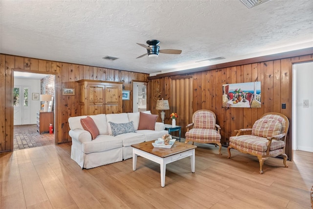 living room with light wood-type flooring, visible vents, ceiling fan, and a textured ceiling