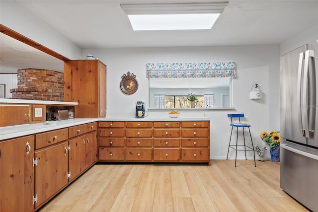 kitchen with brown cabinetry, freestanding refrigerator, light countertops, and light wood-style flooring