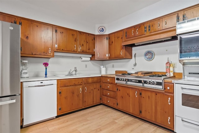 kitchen featuring brown cabinets, stainless steel appliances, light countertops, light wood-style flooring, and a sink