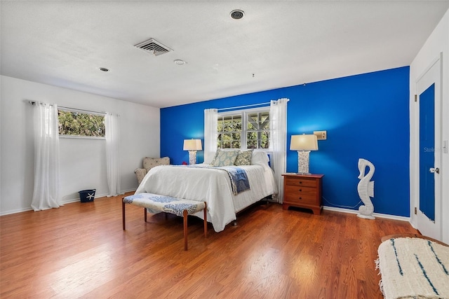 bedroom with visible vents, multiple windows, baseboards, and wood finished floors