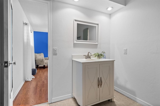 bathroom with a textured wall, vanity, baseboards, and wood finished floors