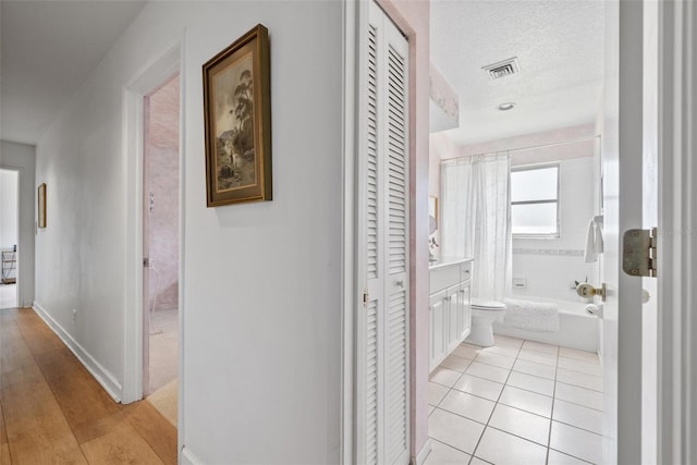 corridor with visible vents, a textured ceiling, baseboards, and light tile patterned floors