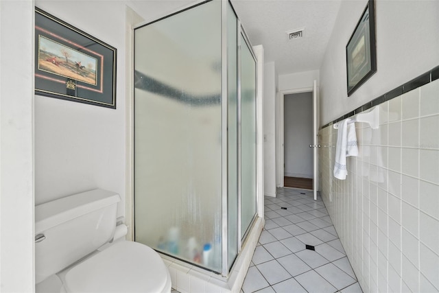 bathroom featuring tile patterned flooring, toilet, visible vents, tile walls, and a stall shower