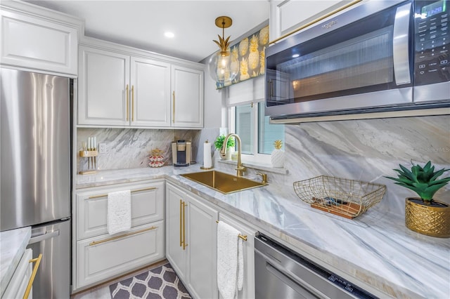 kitchen with pendant lighting, appliances with stainless steel finishes, a sink, and white cabinets