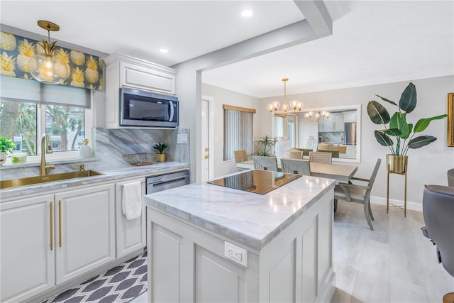 kitchen with black electric cooktop, stainless steel microwave, a sink, and white cabinetry