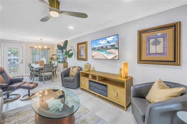 living room featuring baseboards, light wood-type flooring, ceiling fan with notable chandelier, and crown molding