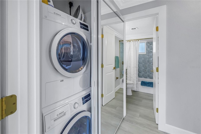 washroom featuring laundry area, stacked washer / dryer, light wood-type flooring, and visible vents