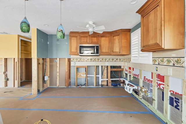 kitchen with ceiling fan, a textured ceiling, hanging light fixtures, brown cabinets, and stainless steel microwave