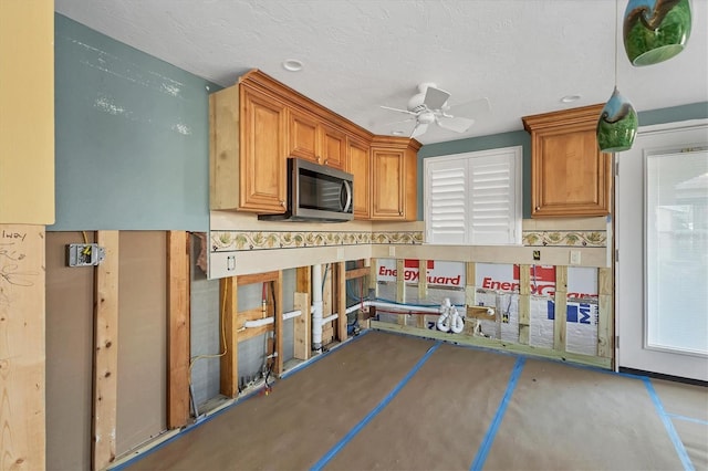 kitchen with a ceiling fan, brown cabinets, stainless steel microwave, and a textured ceiling